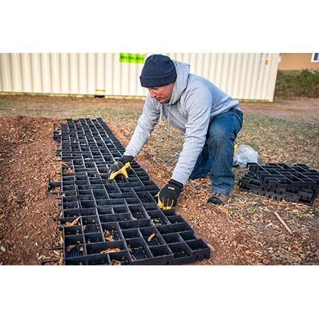 Geobin - Man wearing gloves kneeling outdoors installing black GEOPAVE gravel porous paver panels on ground near a building